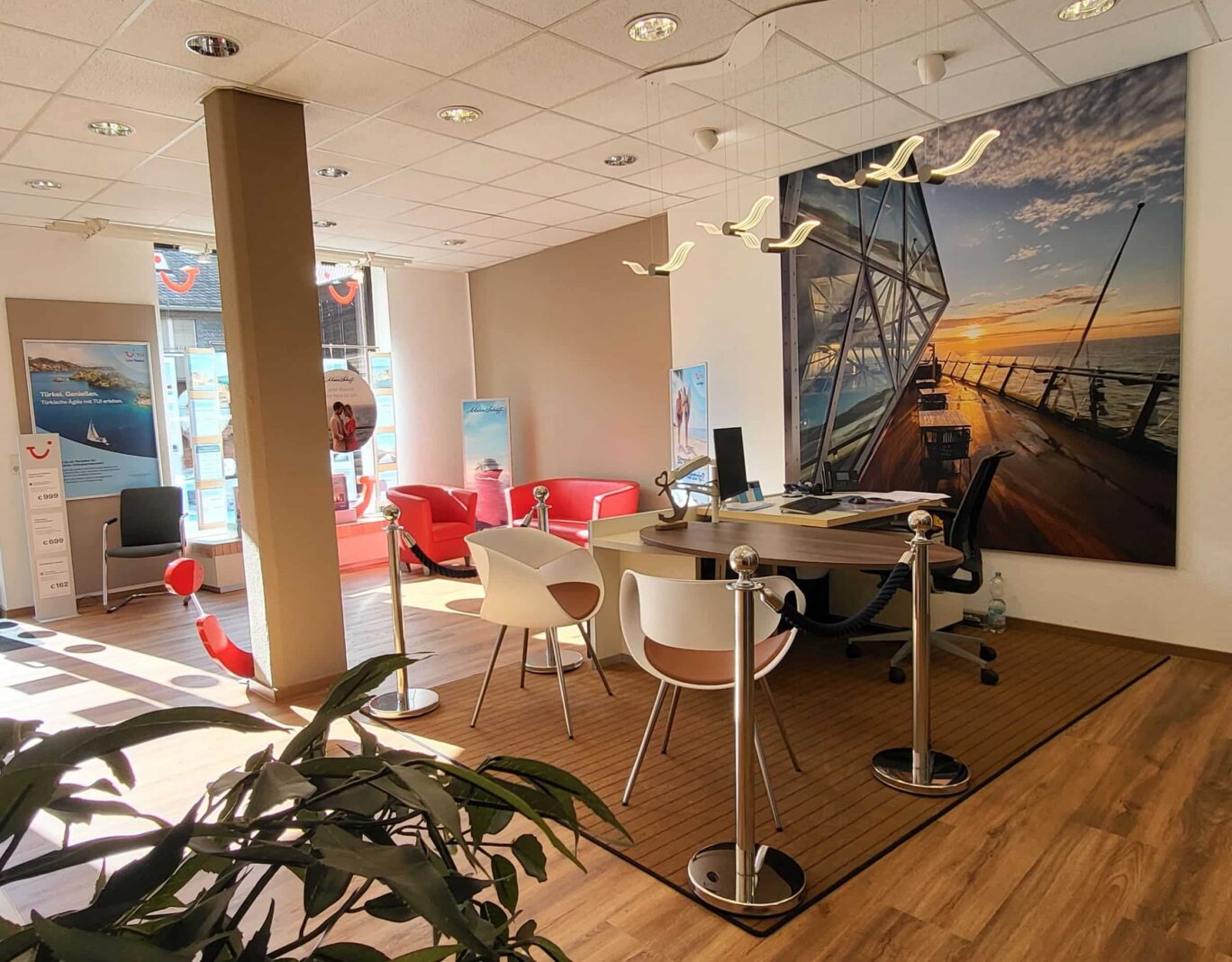 Ankerplatz im TUI Reisebüro Kirchberg, mit Tisch, Stühlen, maritimer Deko und Bildern, sowie Lampen, die aussehen wie Möwen.